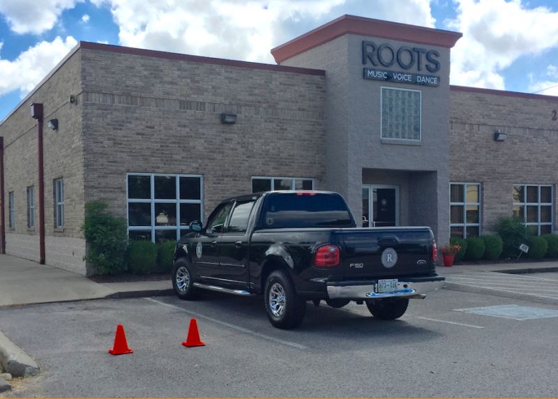 The current ROOTS Academy building, a gray brick facility with a truck parked out front.